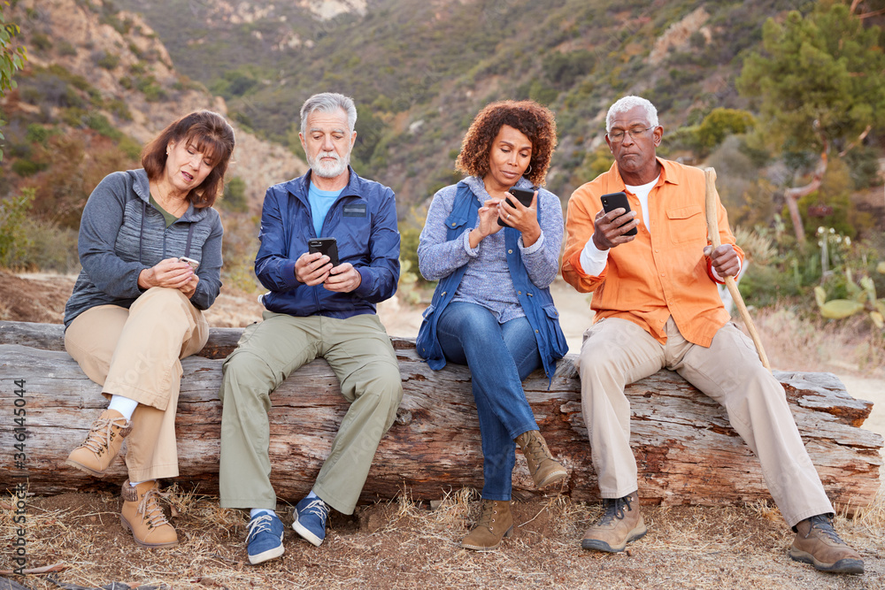 Group Of Senior Friends On Hike In Countryside Checking Mobiles Phones For Fear Of Missing Out