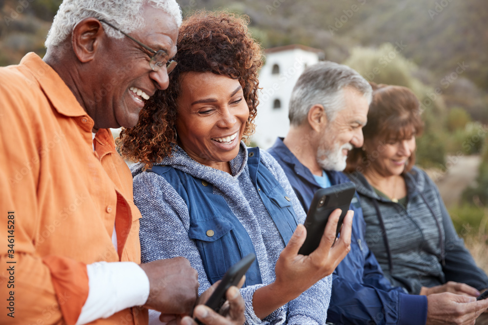 Group Of Senior Friends On Hike In Countryside Looking At Mobiles Phones Together Group Of Senior Friends On Hike In Countryside Looking At Mobiles Phones Together