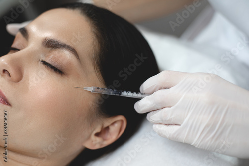 Cut view of young woman lying on therapist's table during botox or collagen injection. Beautician hold neddle carefully at eye wrinkle area.