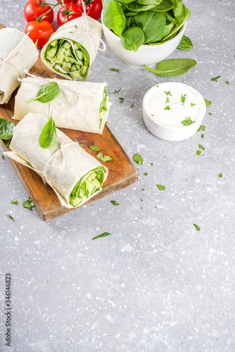 Vegan fresh tortilla wraps with vegetable. Spring fresh pita rolls with tofu, cucumber, baby spinach and avocado. Grey concrete background copy space