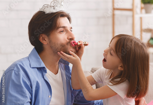 Small girl putting lipstick on her daddy lips