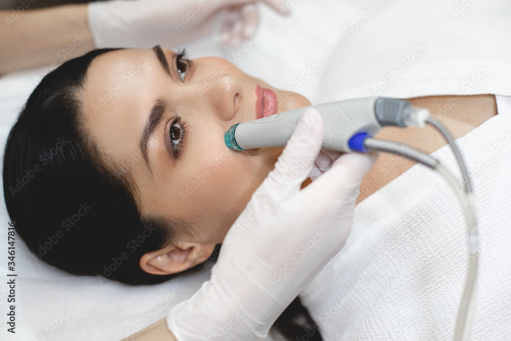 Left side view of young woman lying on cosmetologist's table during rejuvenation procedure with special equipment. Take care about health and youth. Left side view of young woman lying on cosmetologist's table during rejuvenation procedure with special equipment. Take care about health and youth.