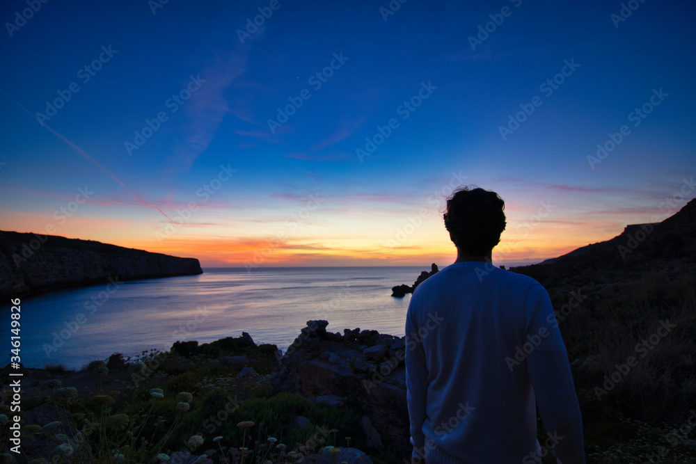 Lone man watching the setting sun from a shoreline. watching beautiful sunset at sea