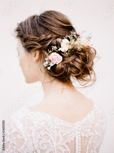Wedding hair style with fresh beautiful flowers. Stylish hairdo on white background. Brunette bride with a bun decorated with white roses.