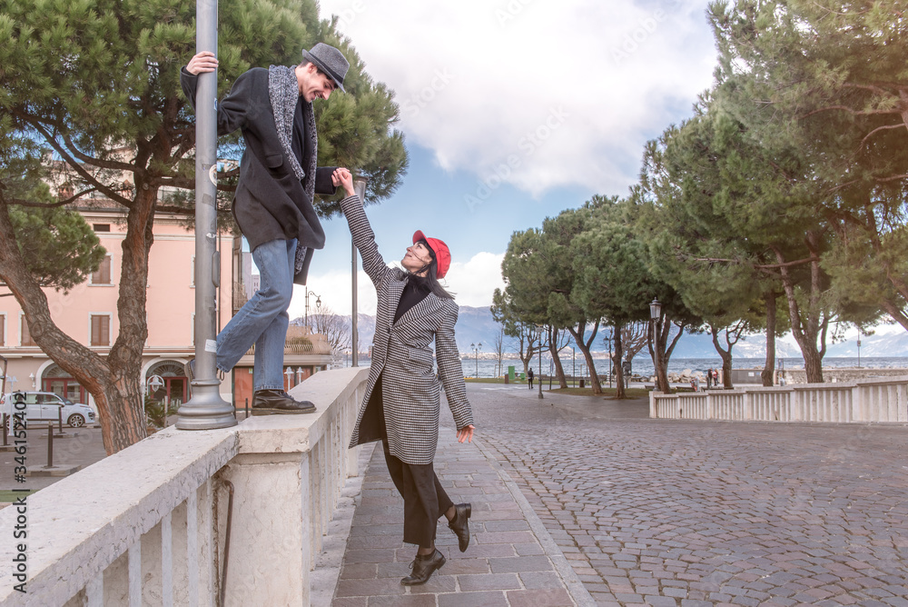 Attractive girl and man play on the bridge. The man got on, the girl remained on the ground. The background of the lake and the mountain. Romantic mood. Couple in love. Street shot.