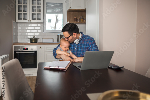 Young father holds his baby boy in his lap and kissing him.