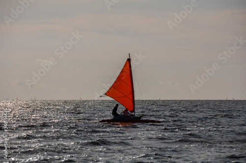 Small romantic yacht with red sail and windsurfers on the background at sunny day