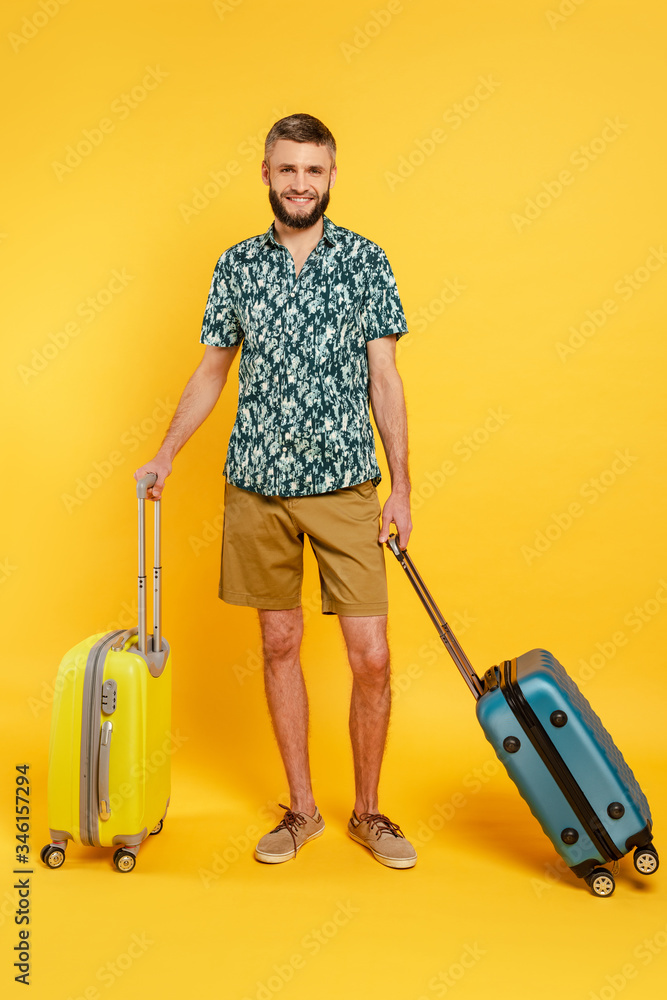 full length view of happy bearded guy with travel bags on yellow full length view of happy bearded guy with travel bags on yellow
