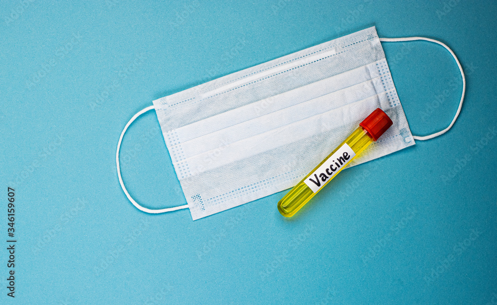 an ampoule containing the covid-19 vaccine, invented to prevent the spread of the virus around the world. medical mask on a blue background an ampoule containing the covid-19 vaccine, invented to prevent the spread of the virus around the world. medical mask on a blue background