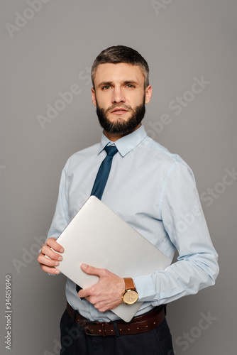 handsome bearded businessman with laptop on grey background