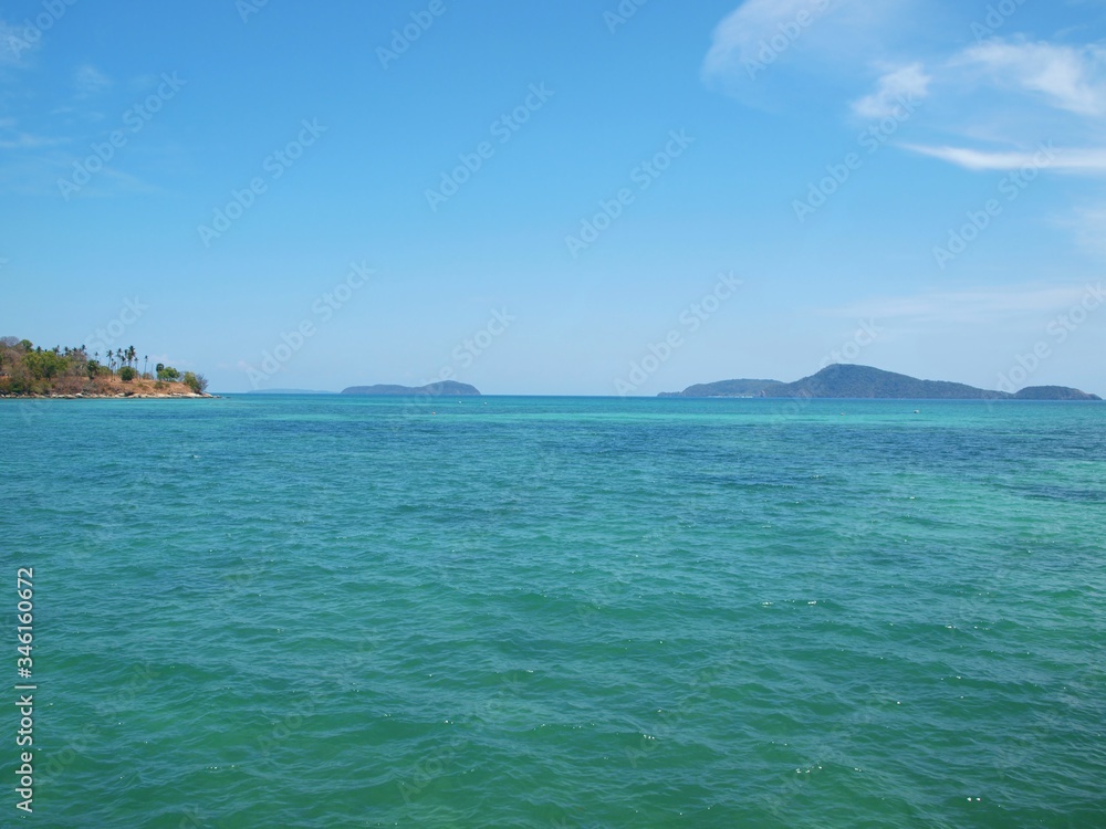 Sea and islands on the horizon. Cliff with palm trees in a distance. Blue sky and transparent white cloud. Azure water with ripples. Thailand resort. Tropical paradise. Seascape. Andaman sea, Phuket. 