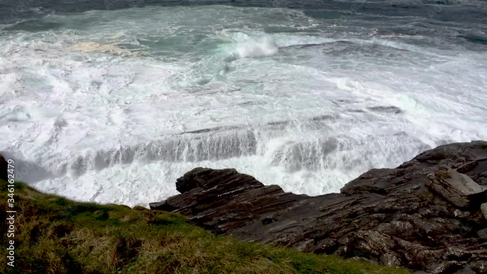Dramatic seascape view of ocean waves crashing on coastal flat rocks near Cliffs of Moher Ireland on sunny summer day. Dramatic seascape view of ocean waves crashing on coastal flat rocks near Cliffs of Moher Ireland on sunny summer day.