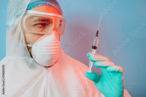 Doctor in protective uniform, reperitor, glasses, gloves on blue background in neon light. close-up portrait of doctor in red neon. tired man is battling coronavirus. syringe with vaccine. covid 19 photo