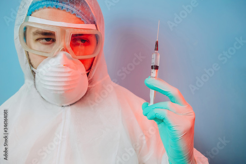 Doctor in protective uniform, reperitor, glasses, gloves on blue background in neon light. close-up portrait of doctor in red neon. tired man is battling coronavirus. syringe with vaccine. covid 19 photo