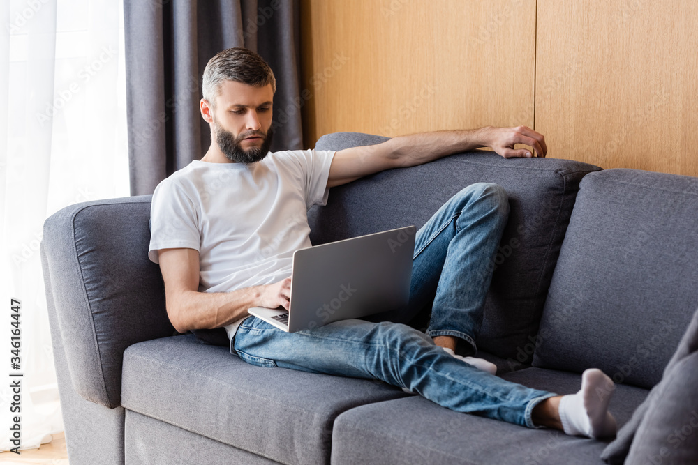 Handsome man working on laptop on couch at home Handsome man working on laptop on couch at home