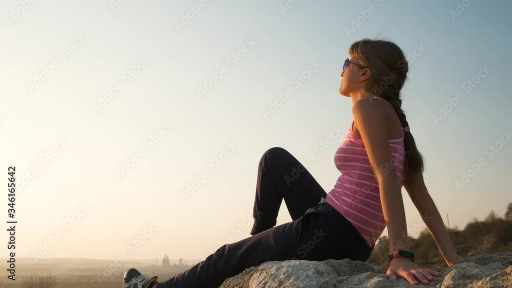 Young relaxed woman sitting outdoors on a big stone enjoying warm summer day. Girl meditating and relaxing on nature at sunset. Young relaxed woman sitting outdoors on a big stone enjoying warm summer day. Girl meditating and relaxing on nature at sunset.