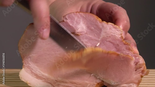 Unrecognizable male hand with knife cutting slicing ham on cutting board. Delicious taste, snacks, cooking process. Healthy food concept. European cuisine, kitchen interior. Close up view