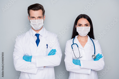 Photo of professional doc guy lady virology clinic avoid contact patients experienced doctors arms folded wear protective facial masks latex gloves lab coats isolated grey color background