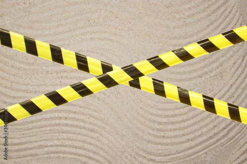 Barrier tape - quarantine, isolation, entry ban. Close up sand beautiful smooth texture on beach in summer sun.