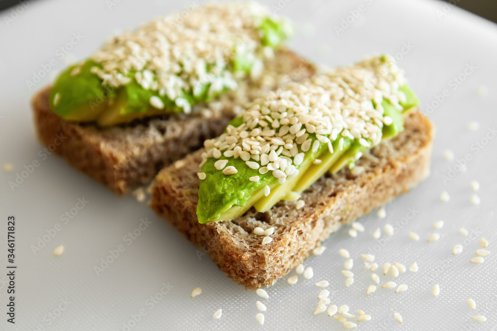 Sandwiches made from avocado and dark sesame bread. On a white plate is a sandwich with avocado and sesame seeds. Sandwiches made from avocado and dark sesame bread. On a white plate is a sandwich with avocado and sesame seeds.