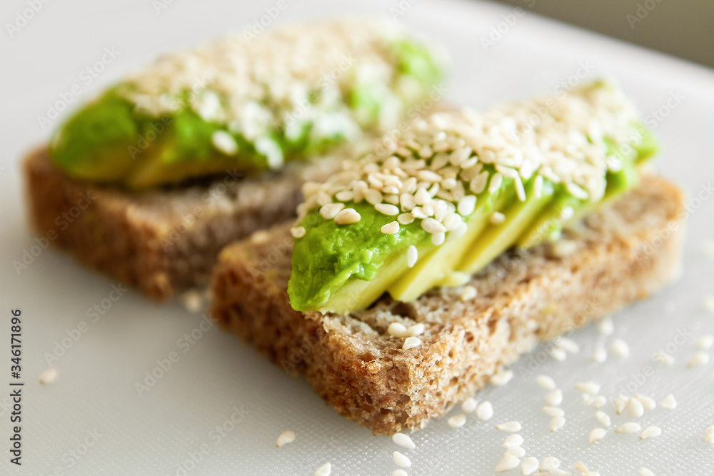 Sandwiches made from avocado and dark sesame bread. On a white plate is a sandwich with avocado and sesame seeds. Sandwiches made from avocado and dark sesame bread. On a white plate is a sandwich with avocado and sesame seeds.