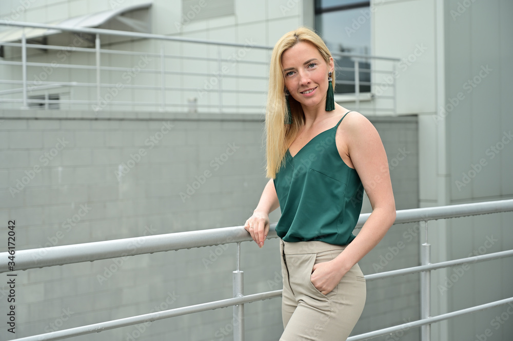Portrait of a young business woman blonde smiling on a background of a city outdoors. Model posing in a green blouse.
