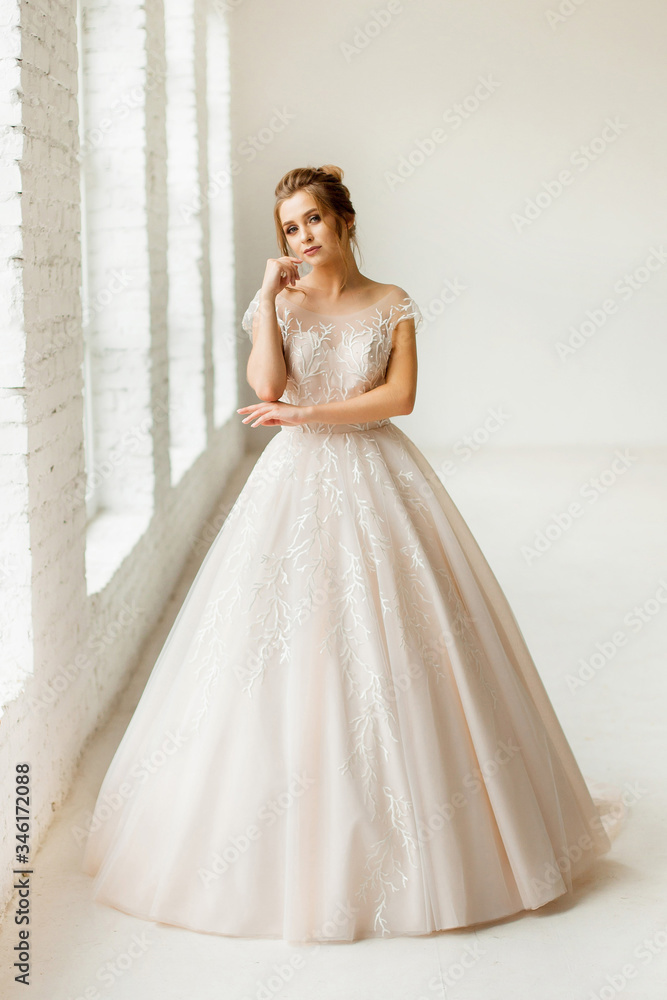 bride in white wedding dress. happy beautiful young woman in white traditional wedding dress on white background. big windows and white walls.