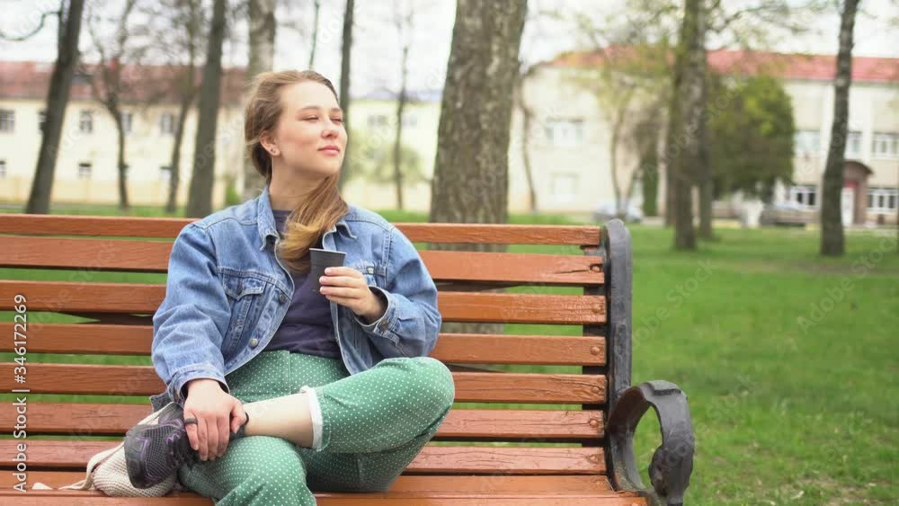Beautiful girl drinking coffee. A girl on a bench in the Park drinking coffee. A blonde woman drinks coffee in a city Park. Beautiful girl drinking coffee. A girl on a bench in the Park drinking coffee. A blonde woman drinks coffee in a city Park.