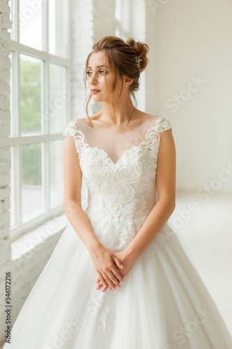 bride in white wedding dress. happy beautiful young woman in white traditional wedding dress on white background. big windows and white walls.