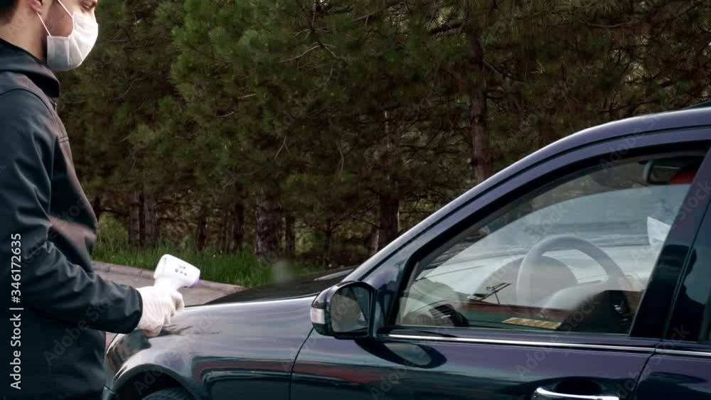Security guy measures a driver's body temperature, fever with an infrared thermometer checking for coronavirus on the road Security guy measures a driver's body temperature, fever with an infrared thermometer checking for coronavirus on the road