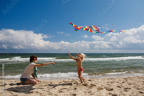 Little Cute Girl with Mother launches a Kite on the Beach by the Sea in Summer. Portrait of a Perfect Happy Family.