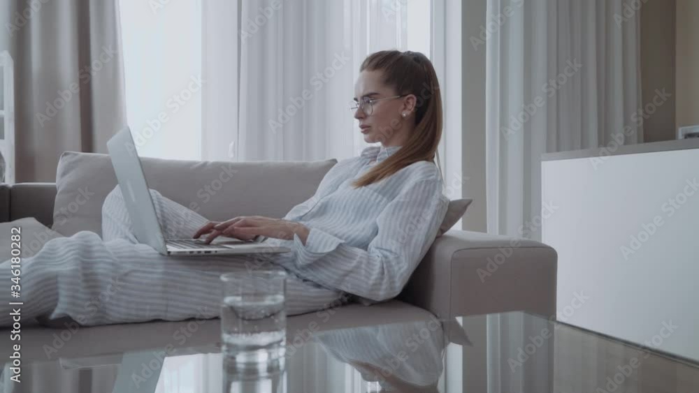 serious attractive young woman sitting on sofa using laptop communicating working online at home, girl typing on computer, enjoying writing blog or chatting serious attractive young woman sitting on sofa using laptop communicating working online at home, girl typing on computer, enjoying writing blog or chatting