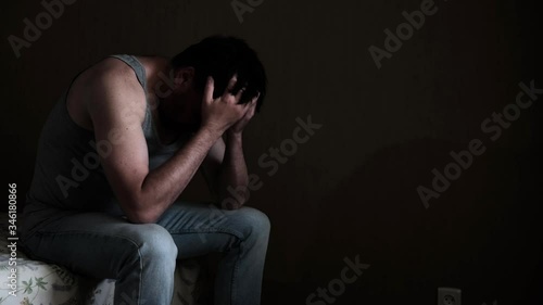 Sad pensive depressed man sitting on a bed in a dark room