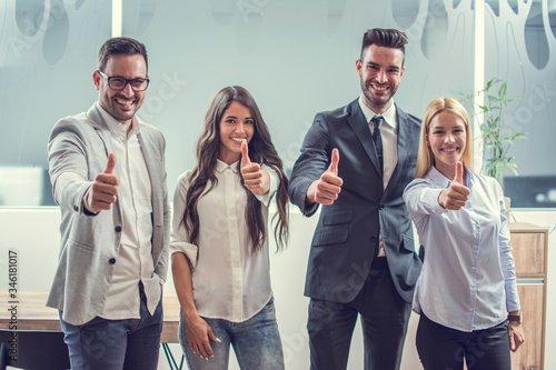 Happy business people showing thumbs up while standing in the office.