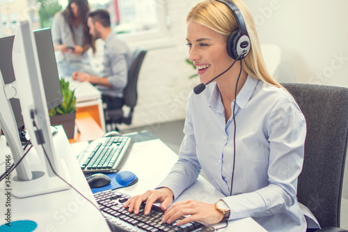 Obraz na płótnie Smiling female helpline operator with headset using computer at office.