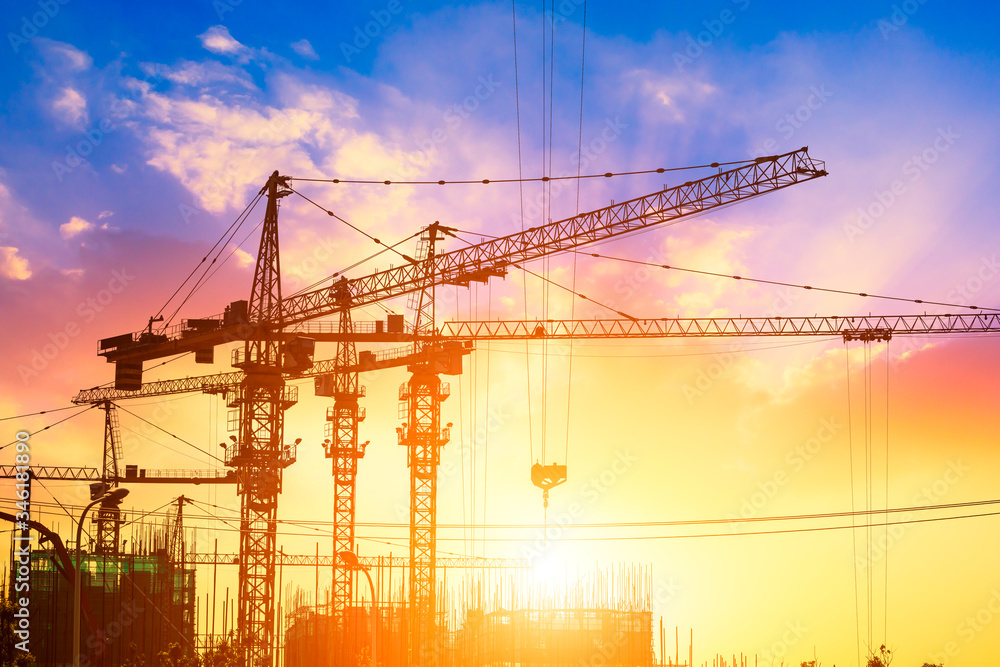 Tower crane and building construction site silhouette at sunrise.