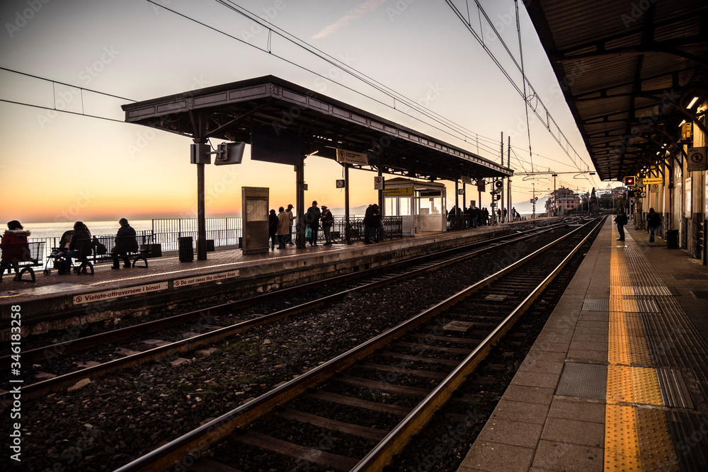 People in a small railway station at sunset in the Mediterranean coast waiting for the arriving train.
