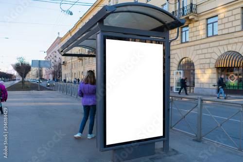 Advertising billboard for one poster at a tram stop. With people sitting waiting for transport.