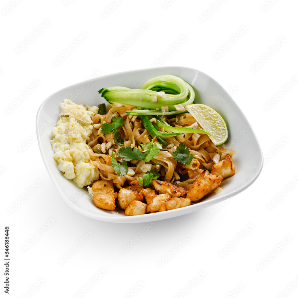 Fried udon noodles in a wok with pieces of pork. Served with tofu cheese, fresh cucumber and lime. Traditional asian food. Isolated on a white background.