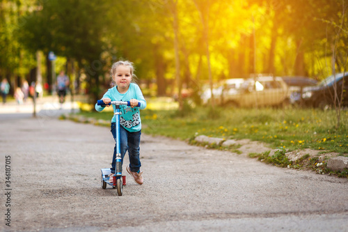 Little beautiful girl on a walk rides a scooter