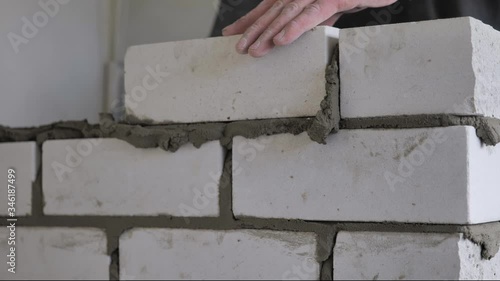 Male hands of a builder lay a brick on fresh wet cement. A row of white brick at a construction site close up view. Wall.