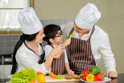 Happy cute little boy with  parents in shef hat cooking  fresh salad  vegetables  in kitchen at home