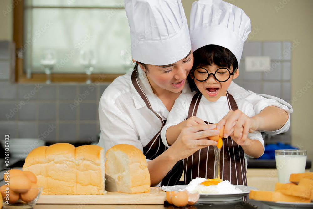 Happy cute asian little boy with mother in apron chef hat preparing baking the dough in kitchen room at home Happy cute asian little boy with mother in apron chef hat preparing baking the dough in kitchen room at home