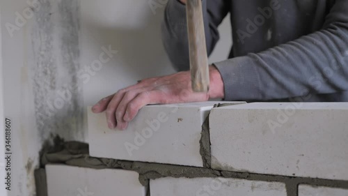 Male hands of a builder lay a brick on fresh wet cement. A row of white brick at a construction site close up view. Wall.