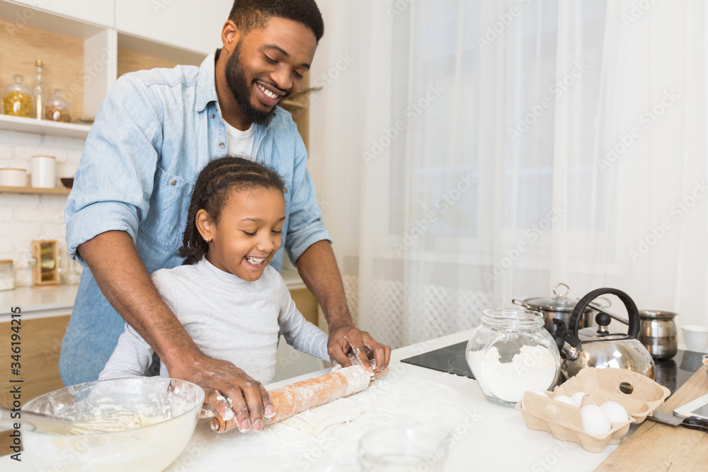 Smiling african father and daughter rolling dough together Smiling african father and daughter rolling dough together