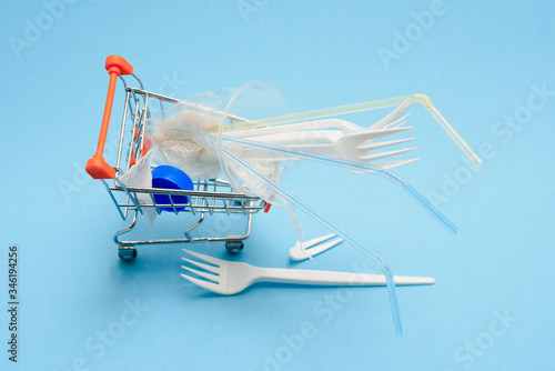 disposable plastic white plug, and bottle in a shopping trolley on a blue background copy space, zero waste life style concept, garbage for recycling, eco consciousness