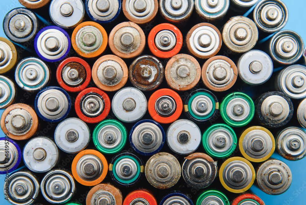 Close up of positive ends of colorful discharged batteries of different sizes and formats, top view, copy space. Used alkaline battery on concrete background. Hazardous garbage concept.