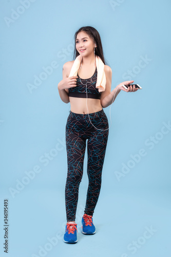 An Asian girl wearing a leggings and plugging in a phone earphone to exercise on a pastel blue studio scene. photo