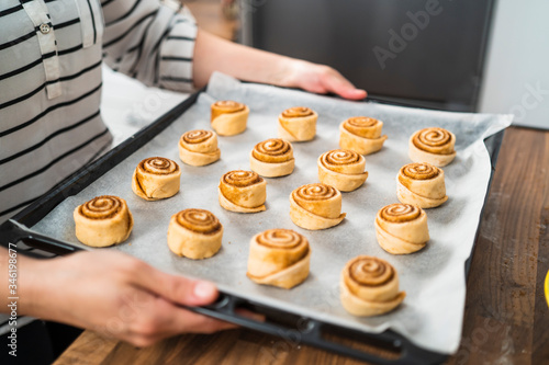 Close up of a woman with a tray of raw homemade cinnamon rolls ready to bake.