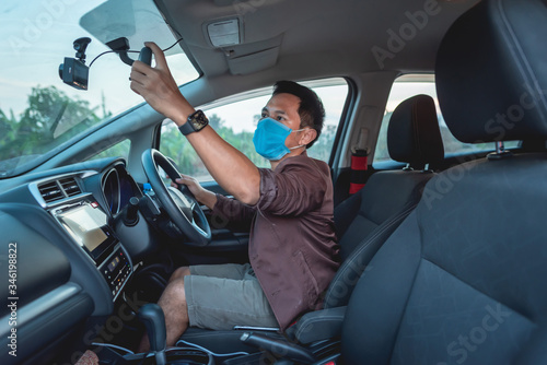 A man sat in a car and had a protective mask. He is looking at the rear view mirror of the car. © Wutthichai